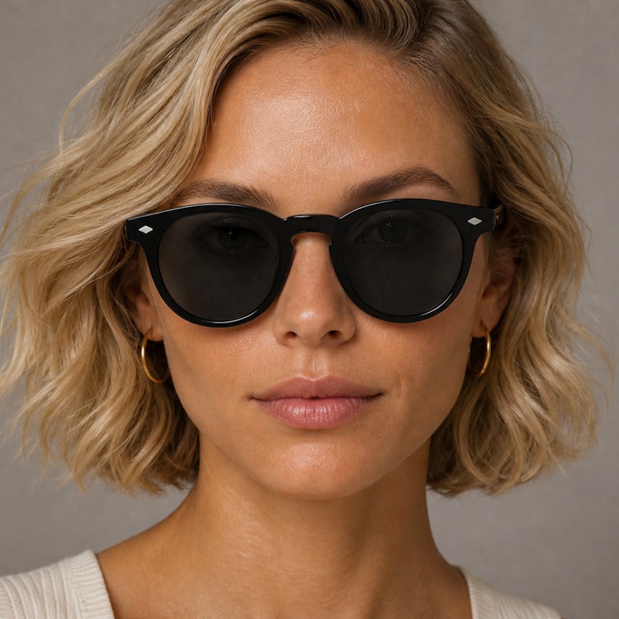 Woman with short blonde hair wearing round black plastic sunglasses