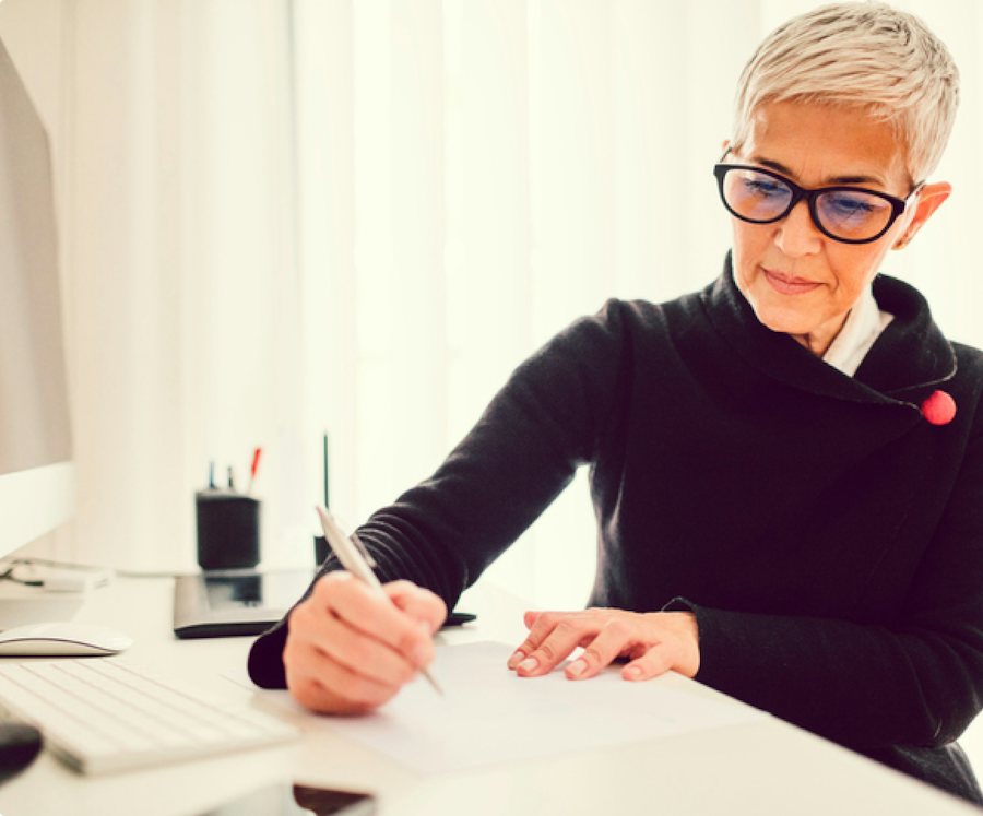 Older lady with short blonde hair working at a desk wearing black glasses