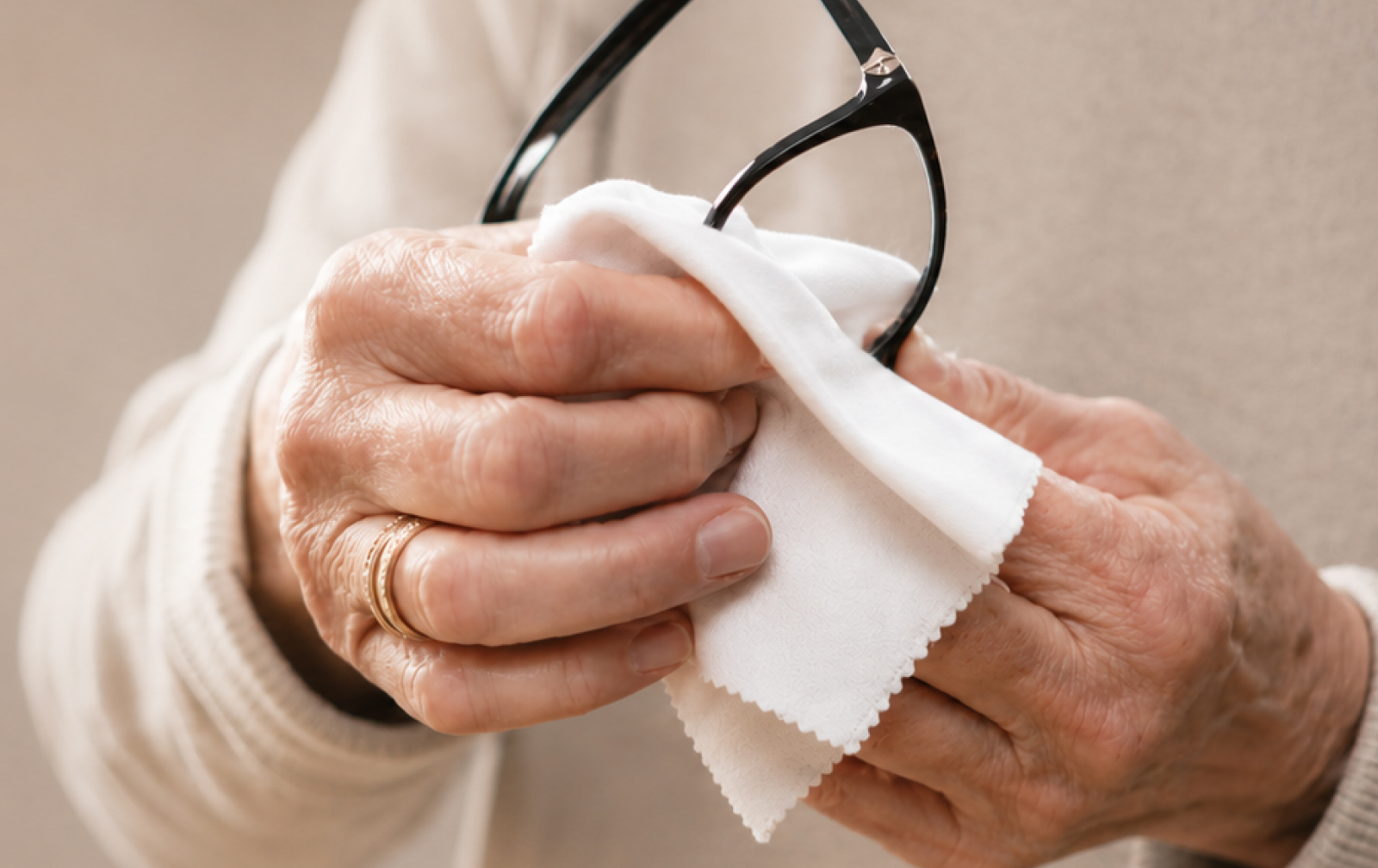 Hands holding a pair of glasses cleaning the lenses with a microfibre cloth