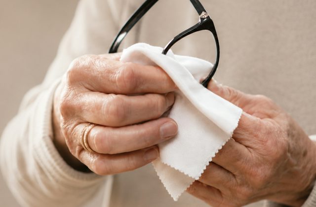 Hands holding a pair of glasses cleaning the lenses with a microfibre cloth