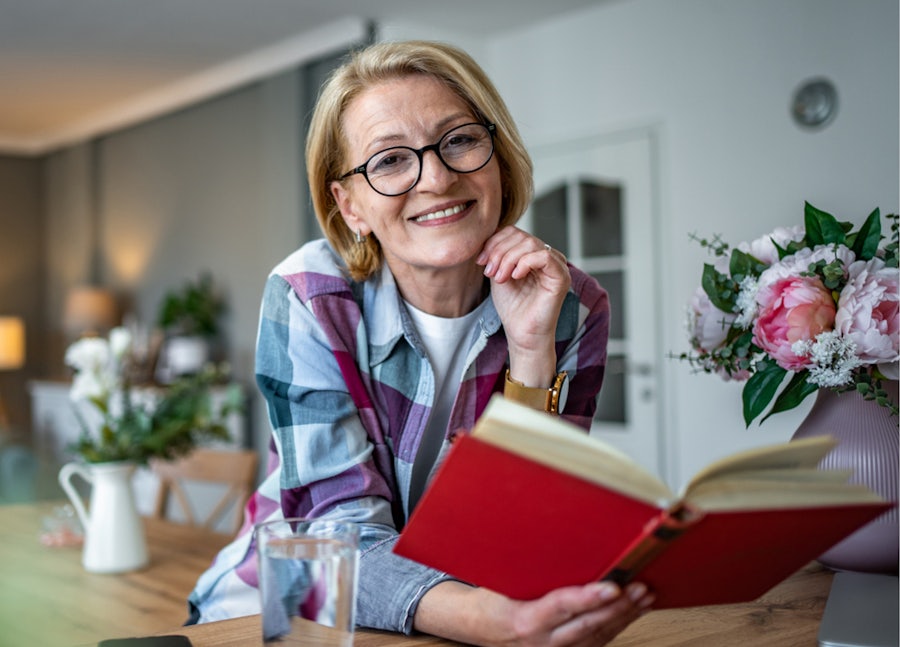 Woman smiling holding a book wearing reading glasses