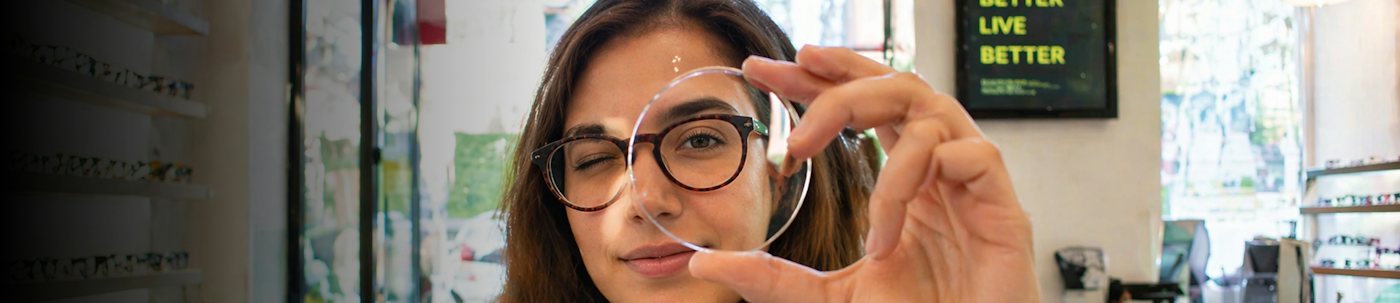 Woman holding up an optical prescription lens infront of her eye