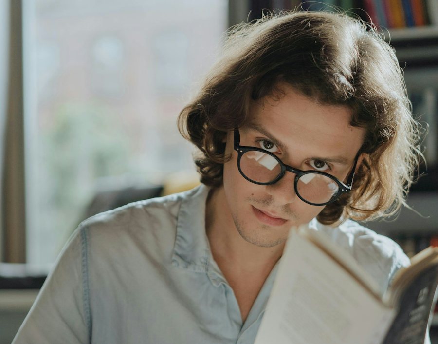Man with long hair in a library reading wearing reading glasses