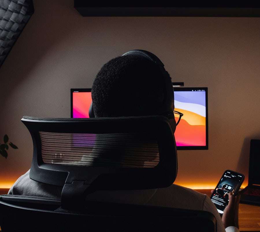 Man wearing gaming glasses in front of his computer looking at his phone