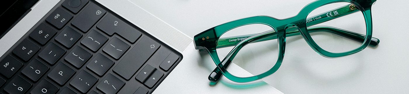 A pair of green plastic glasses resting on the edge of a laptop