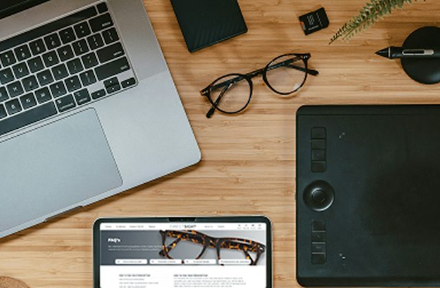 Glasses sat on a desk next to a laptop, track pad and ipad