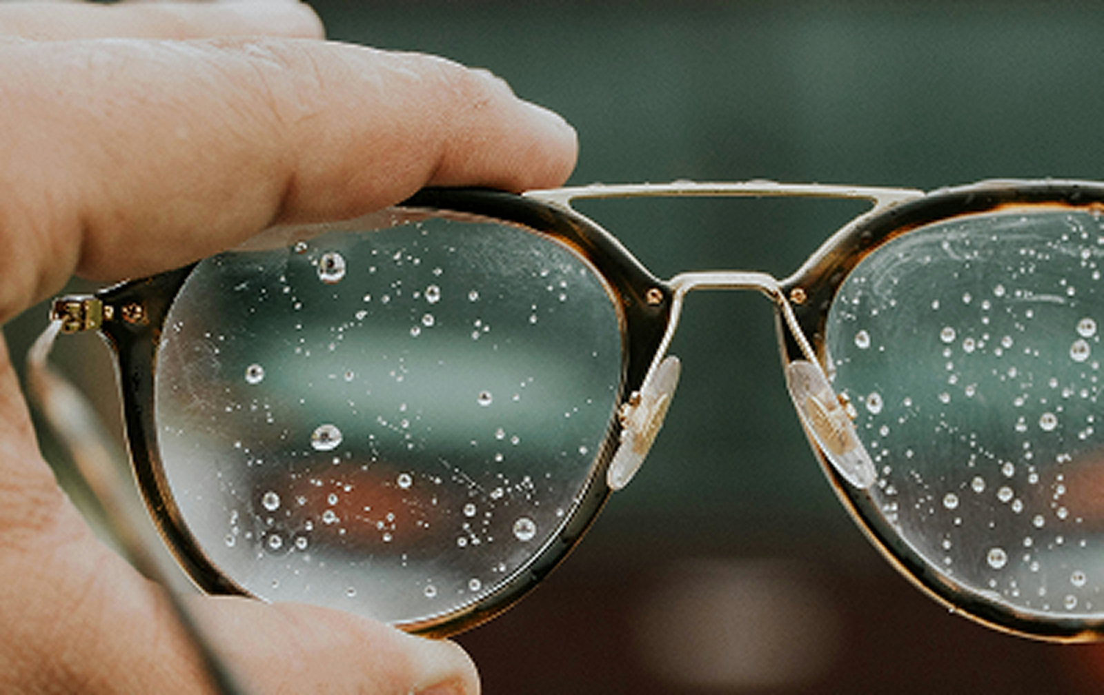 A hand holding a pair of glasses that have water running down the lenses