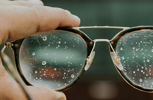 A hand holding a pair of glasses that have water running down the lenses