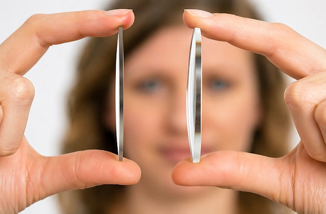 Woman holding two optical lenses highlighting the difference between standard thickness and high index lenses
