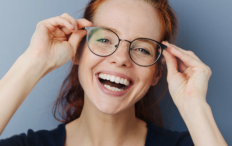Woman with red hair smiling holding onto her eyeglasses