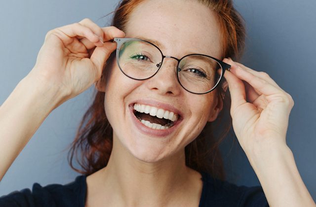Woman with red hair smiling holding onto her eyeglasses
