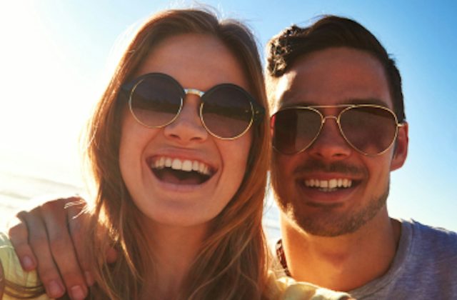 Attractive couple wearing sunglasses smiling into the camera
