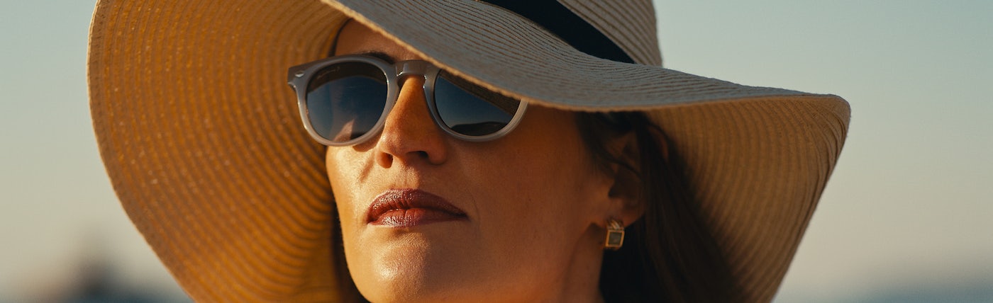 Woman on a beach wearing a large sun hat and a pair of grey sunglasses