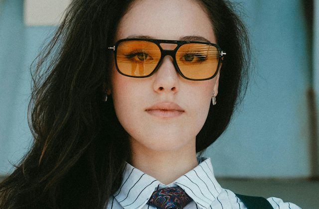 Woman wearing aviator inspired black plastic glasses with amber tinted lenses