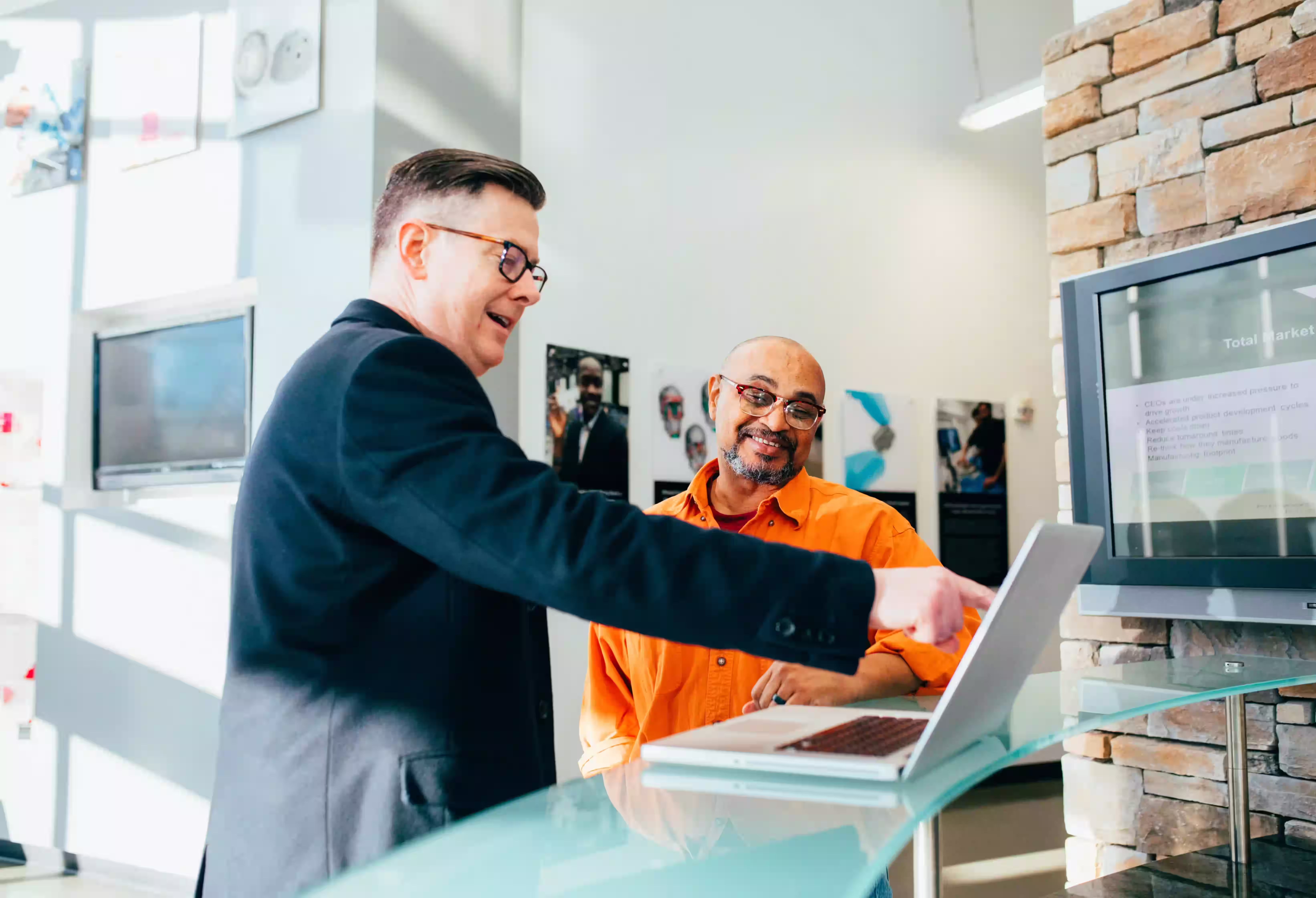 Business professional pointing at laptop while discussing project with client in modern office lobby