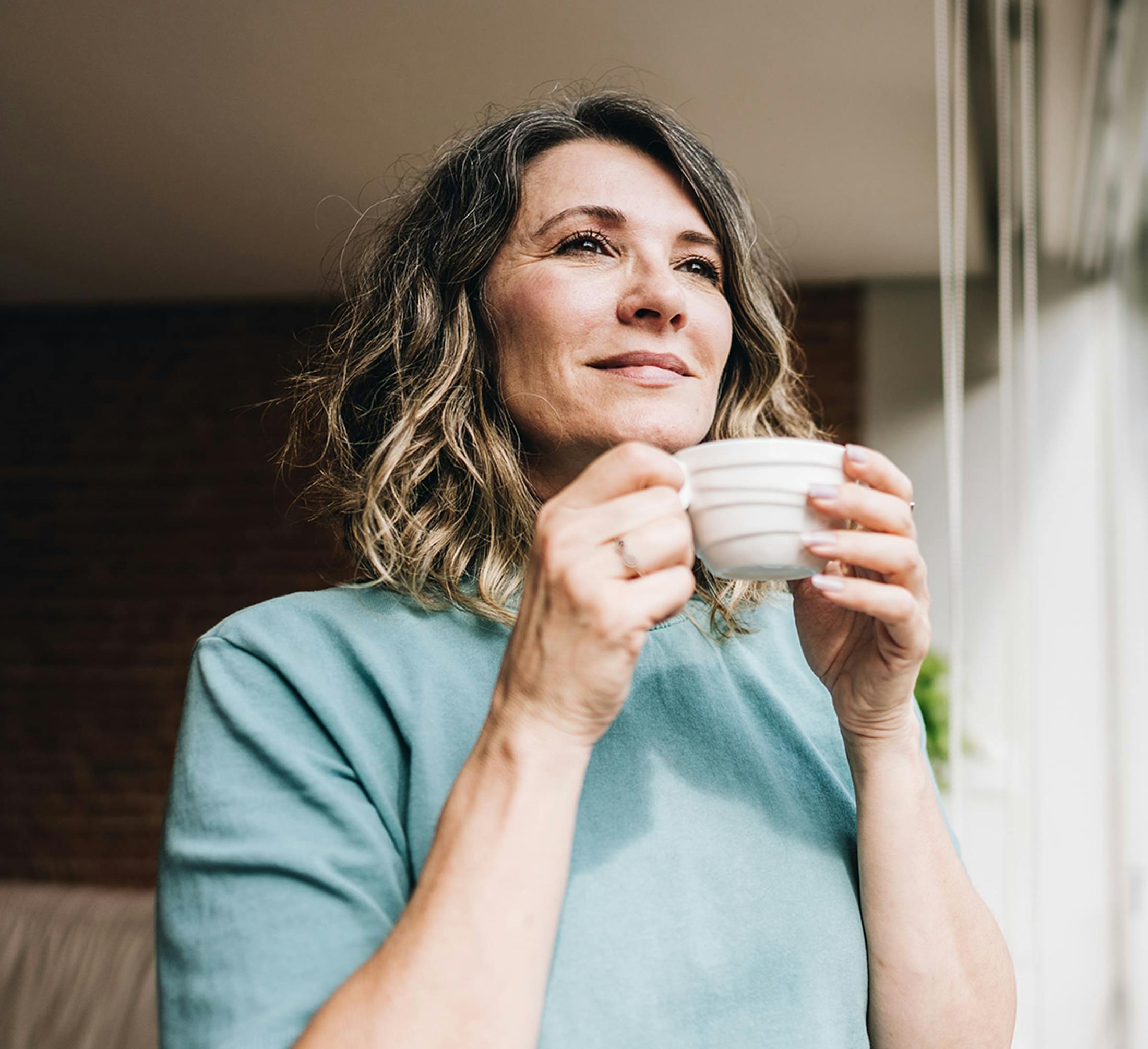 woman holding a mug while looking out the window