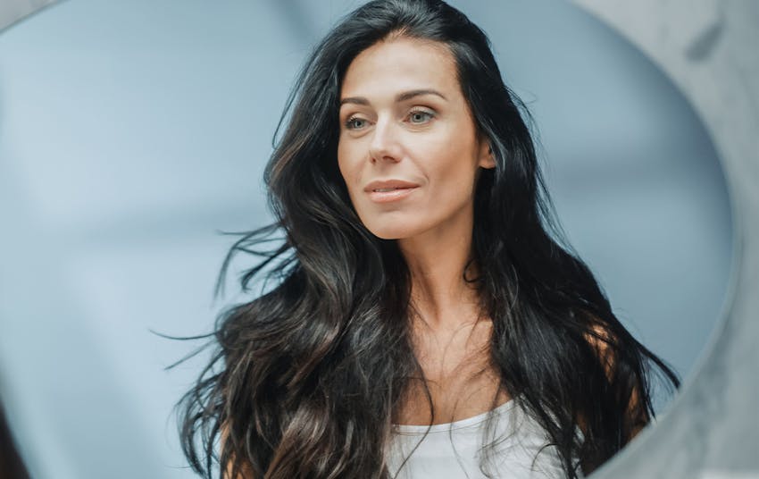 woman with long black hair looking into a mirror