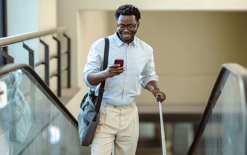 man on phone going up escalator with suitcase