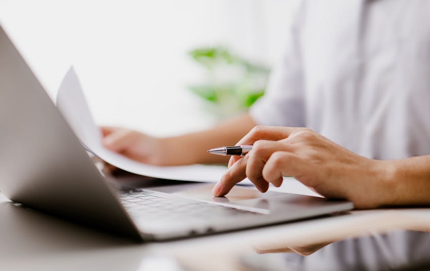 person on their laptop with pen and paper