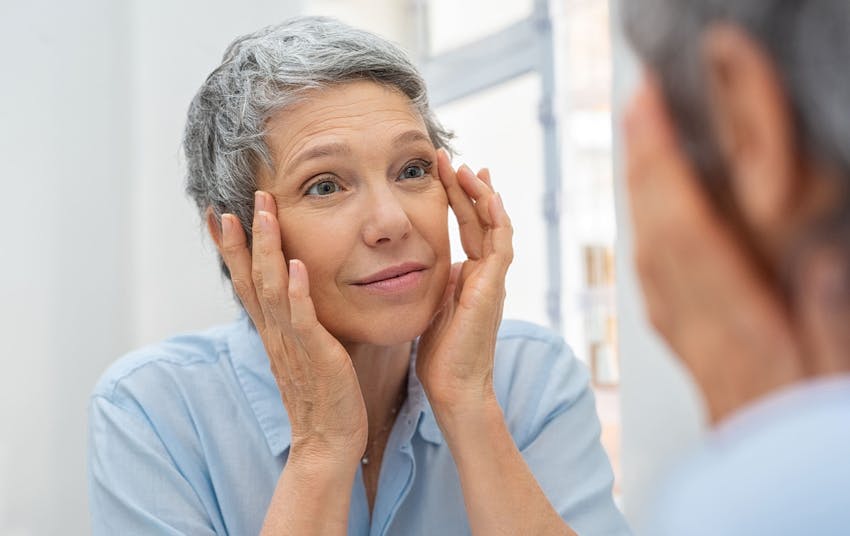 woman touching around her eyes looking in mirror