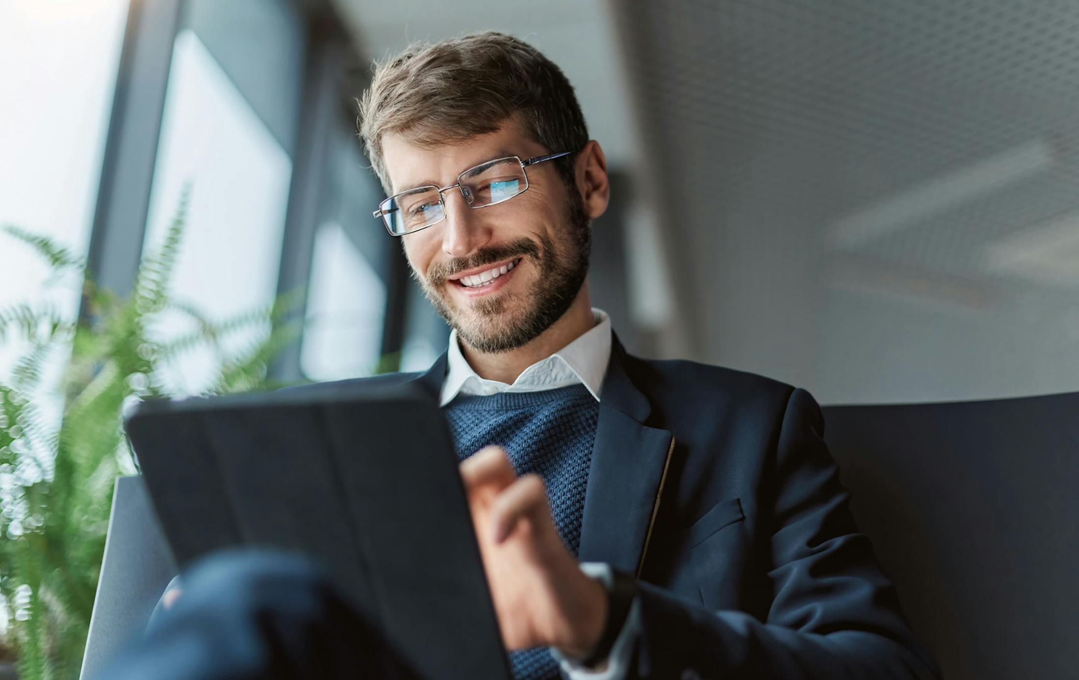 man smiling sitting down in suit with ipad in hand