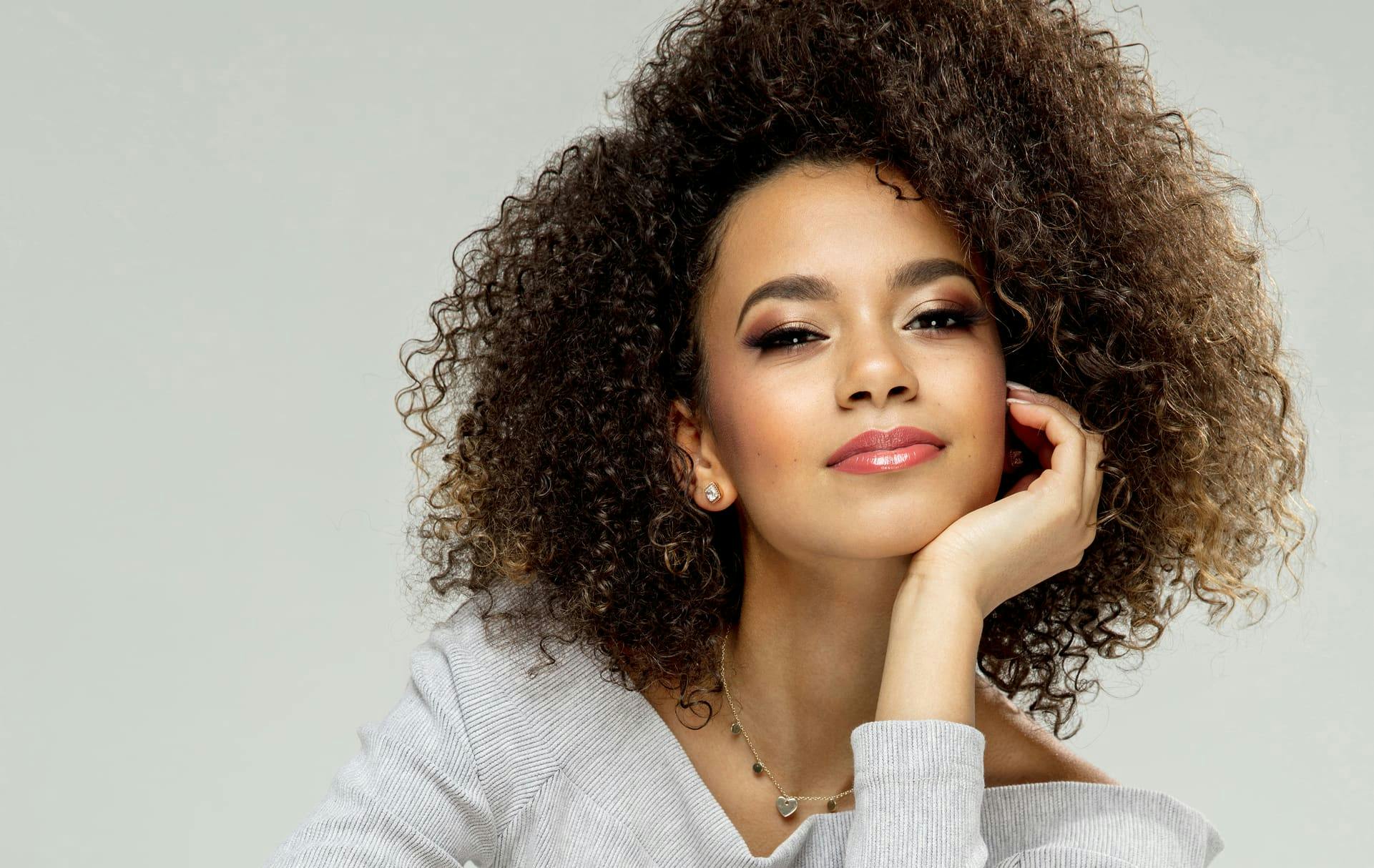 Woman with curly hair smiling while resting chin on hand