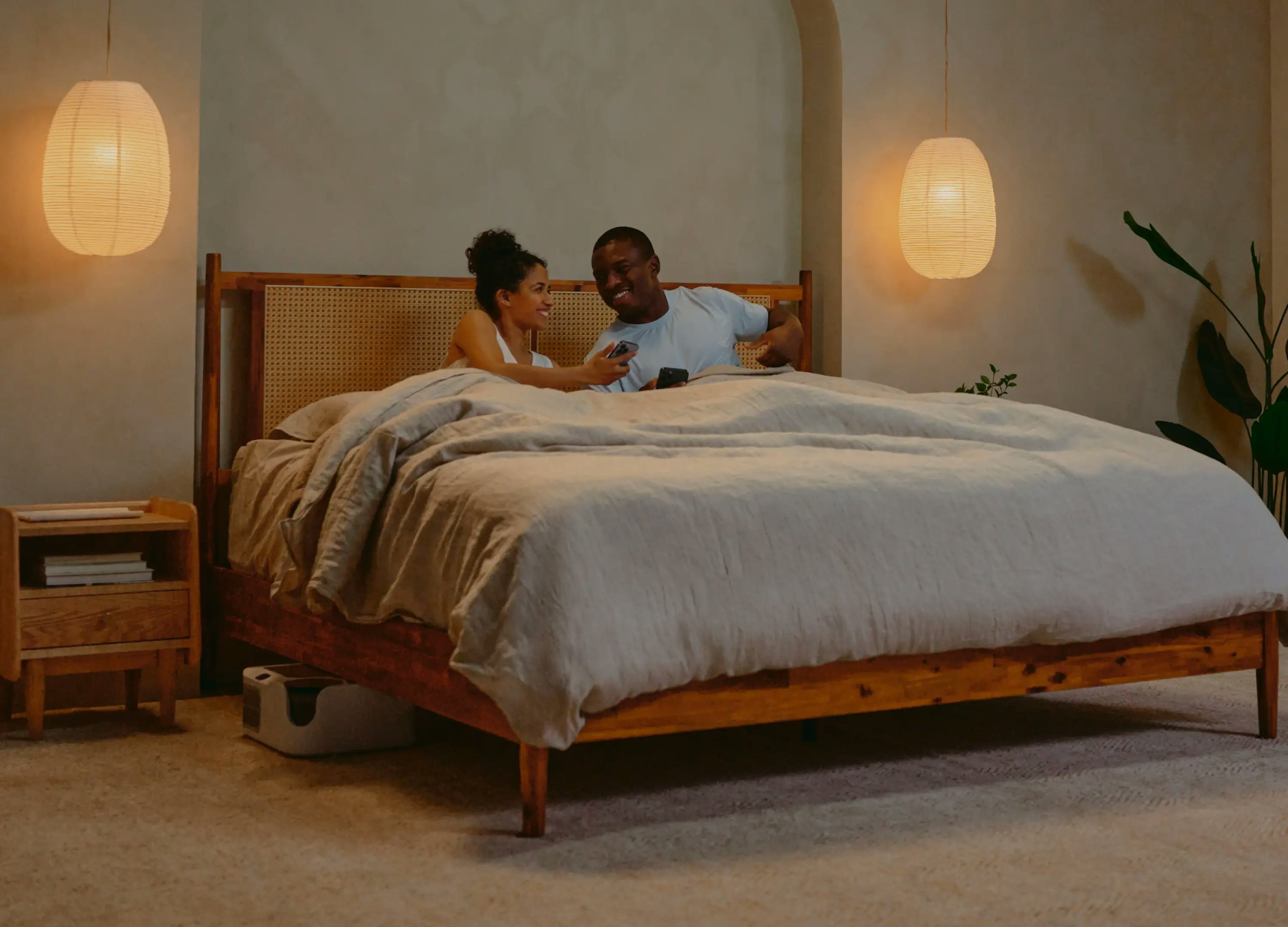 Couple adjusting sleep temperature settings on phones while relaxing in bed Couple adjusting sleep temperature settings on phones while relaxing in bed