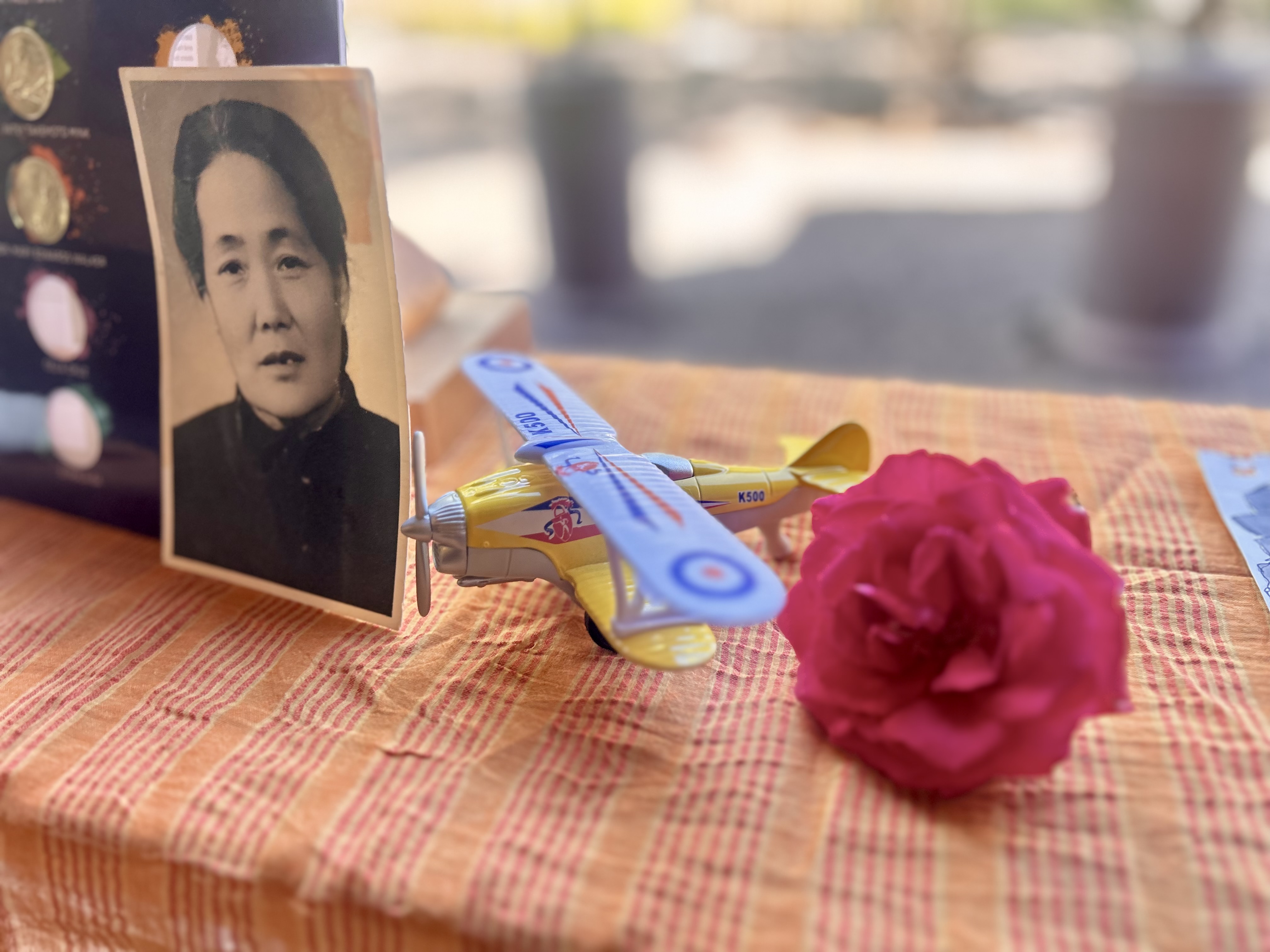A black and white picture of a woman, a toy plane and a rose next to each other on a table
