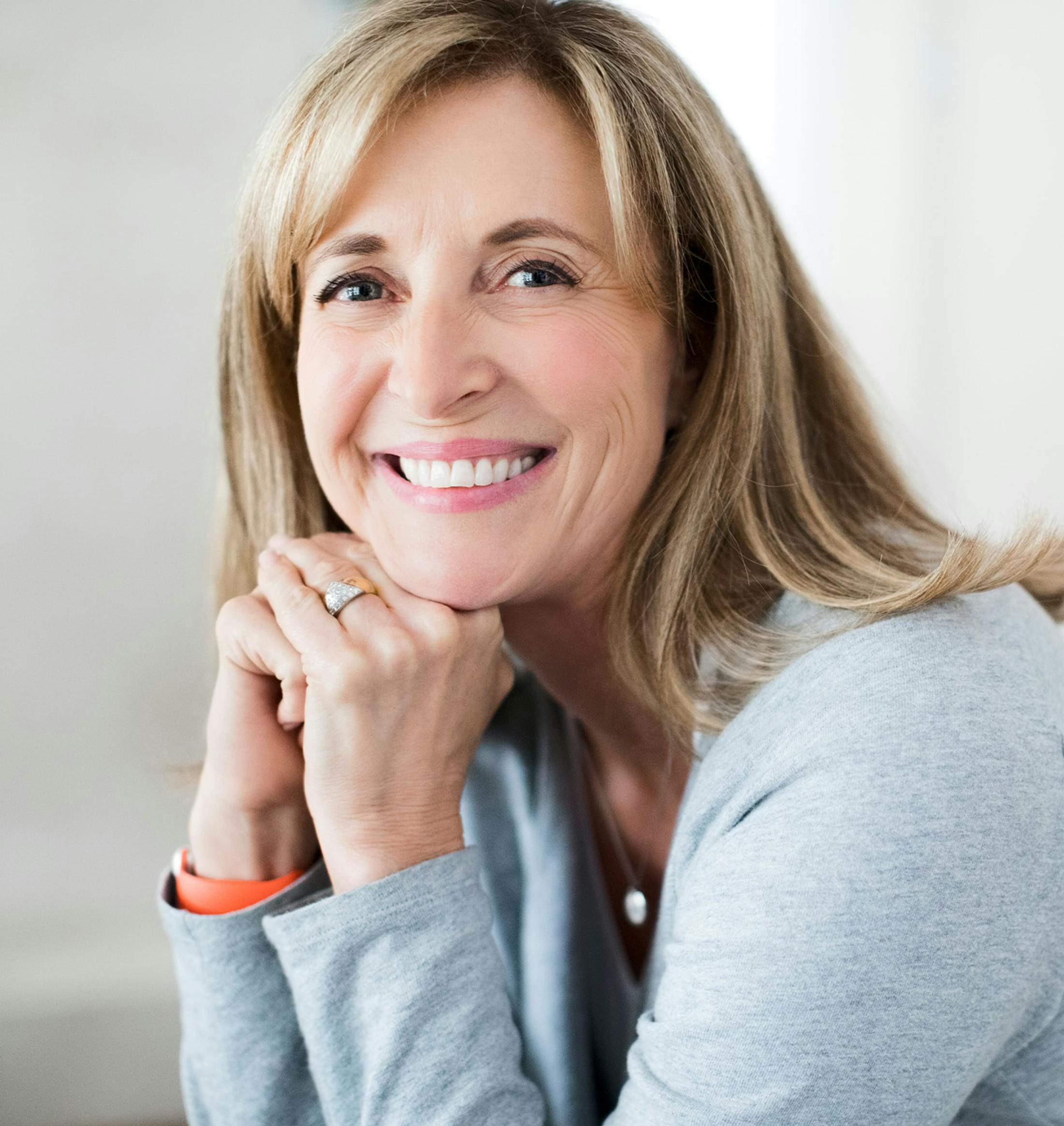 older woman smiling with her hands under her chin