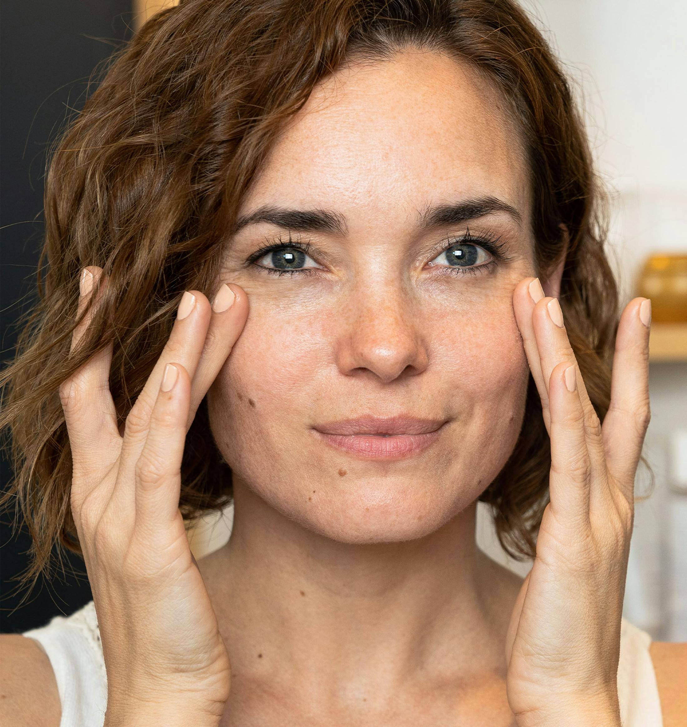 woman with short brown hair touching around her eyes