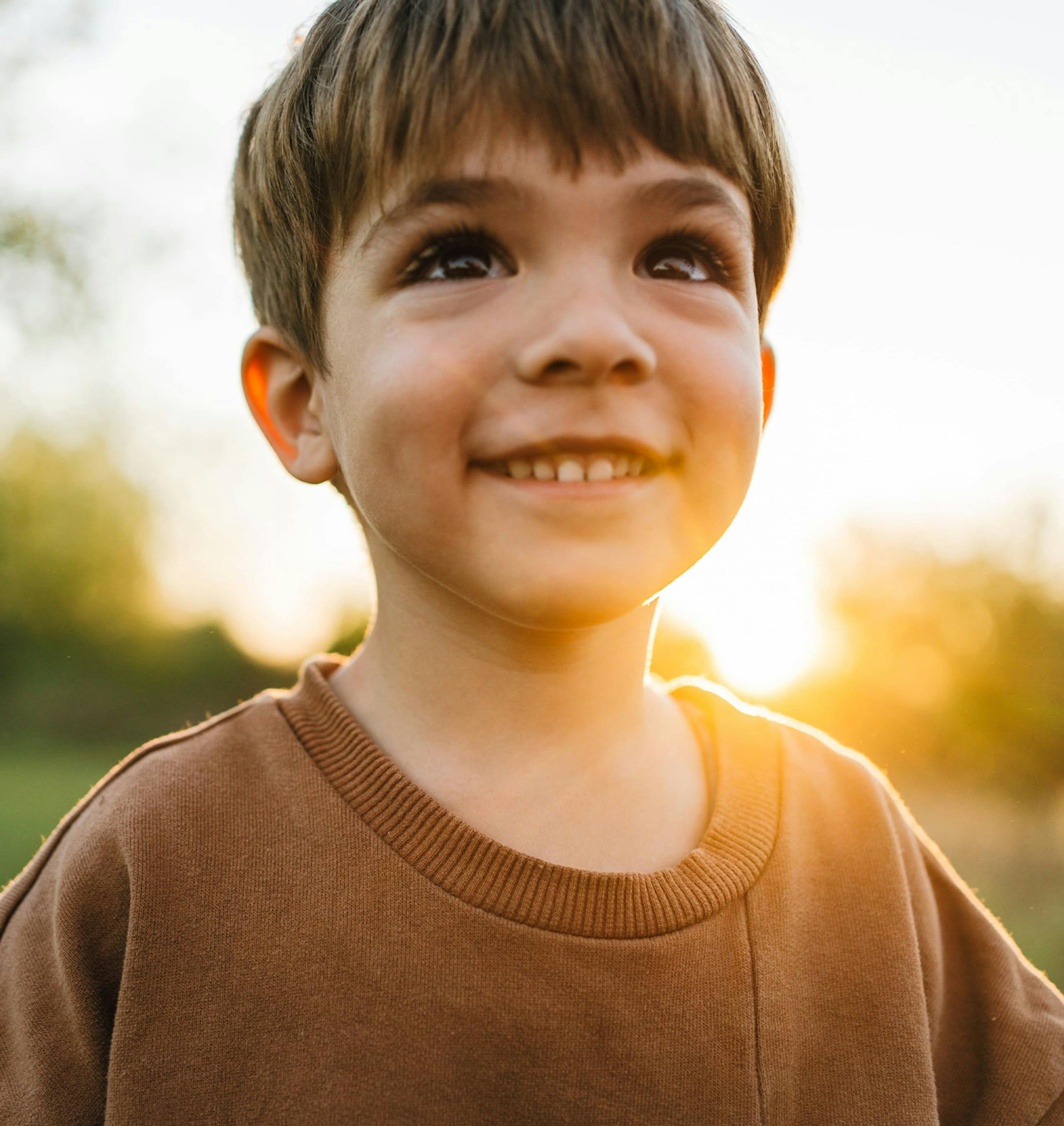 little boy outside with sunset behind him