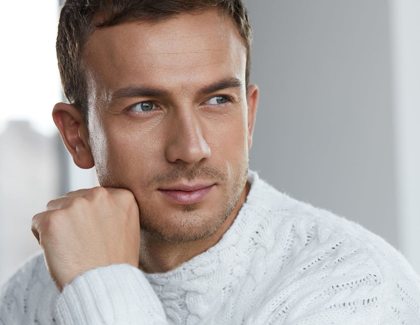 man in white sweater with fist on his jaw