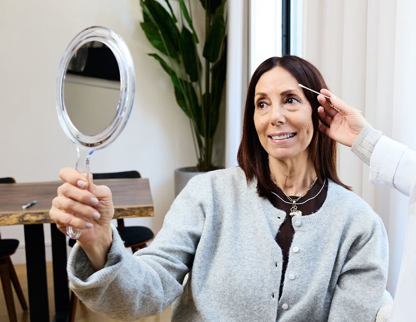 female patient smiling in handheld mirro while getting her eyes checked