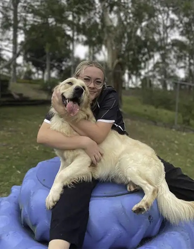 Smiling staff member cuddling a happy Golden Retriever during Doggy Daycare at Pet Resorts Australia Samford, a leading dog resort offering outdoor play, personalised attention, and quality dog daycare in Samford.