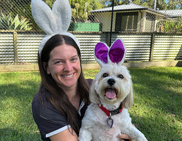 A caring pet nanny holding a dog, both wearing easter bunny ears at doggy daycare in Kangy Angy