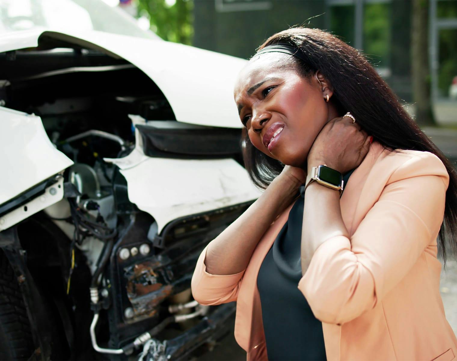 woman, standing next to a car wreck, holding her neck in pain