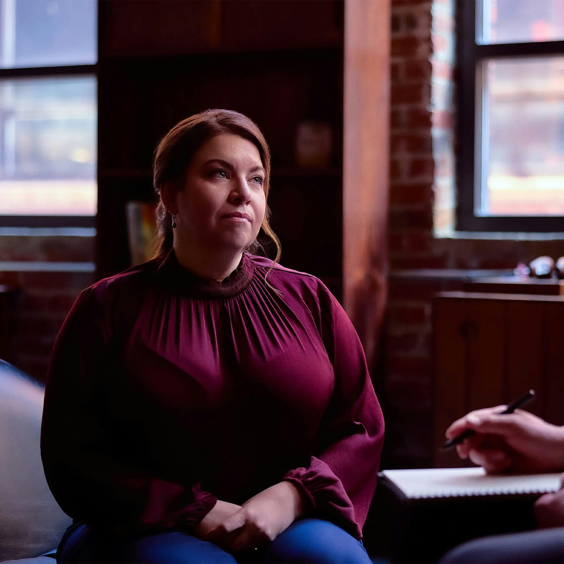 woman looking at a person who is writing on a paper