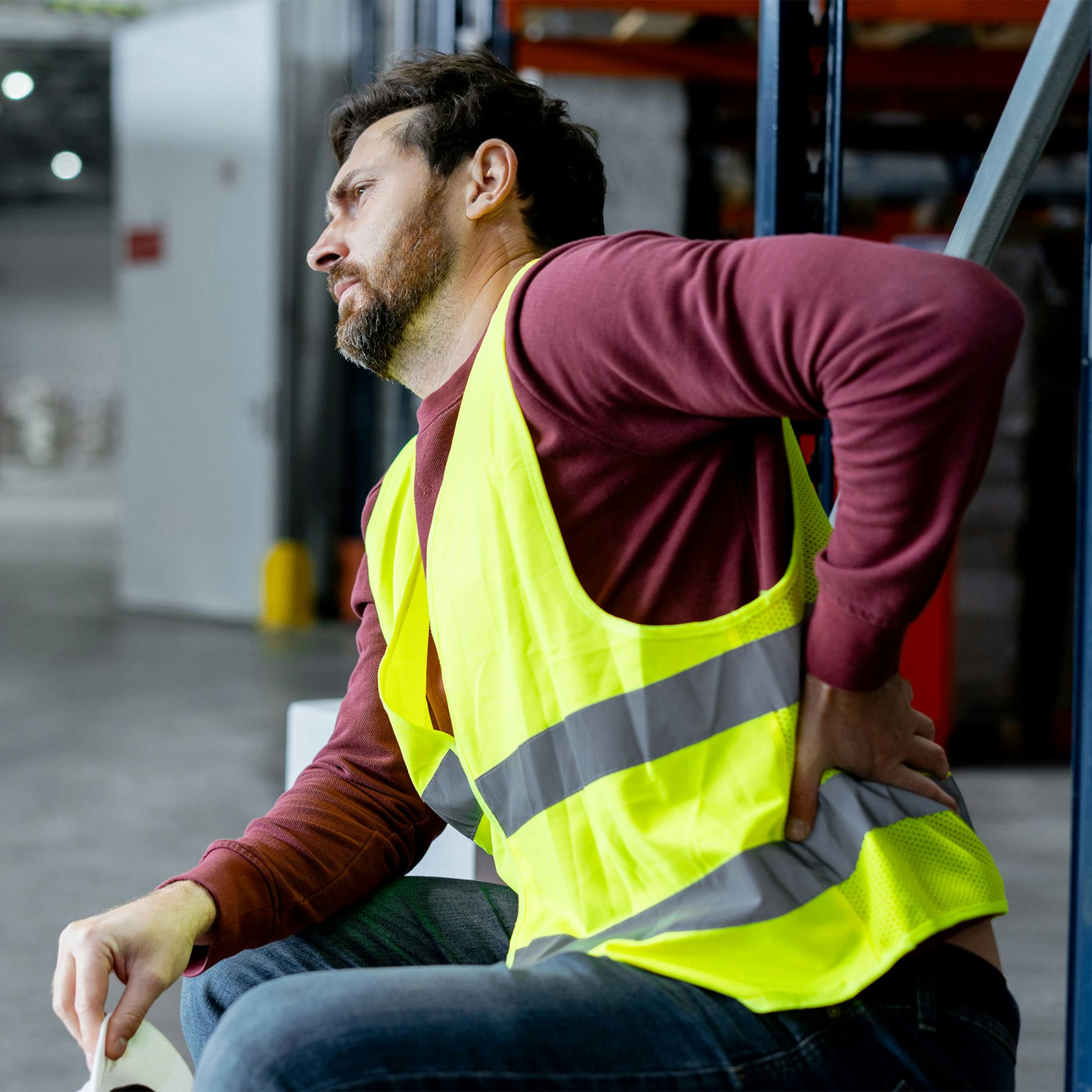 man in a neon vest, holding his lower back in pain