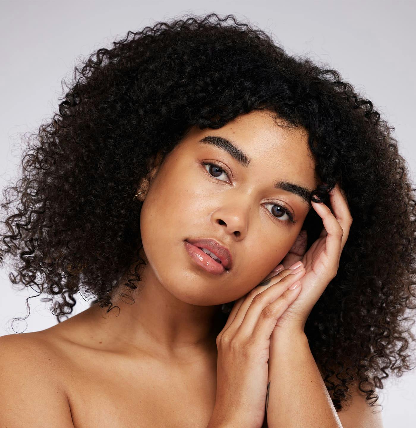 Woman with curly hair holding hands up near face