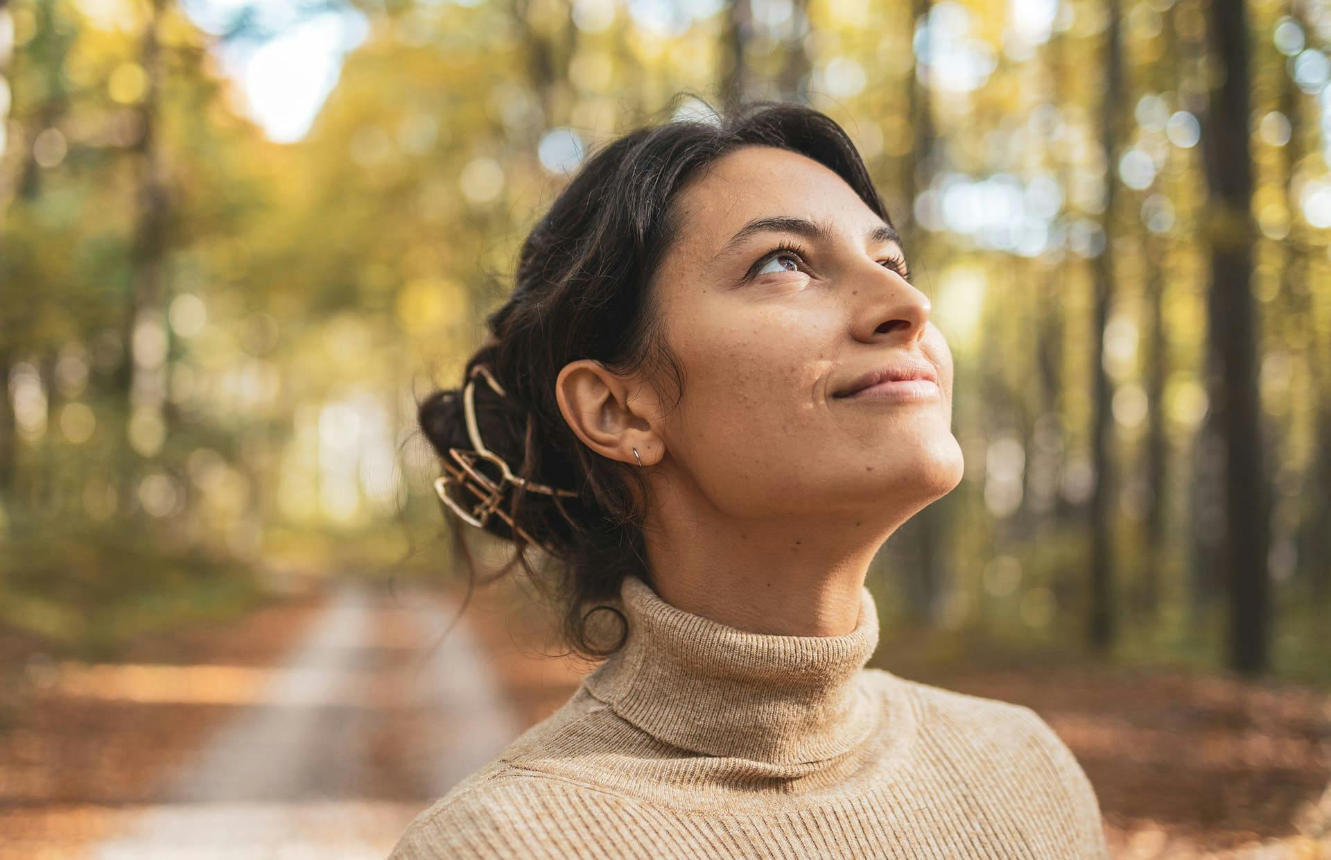 Woman smiling while looking up at trees