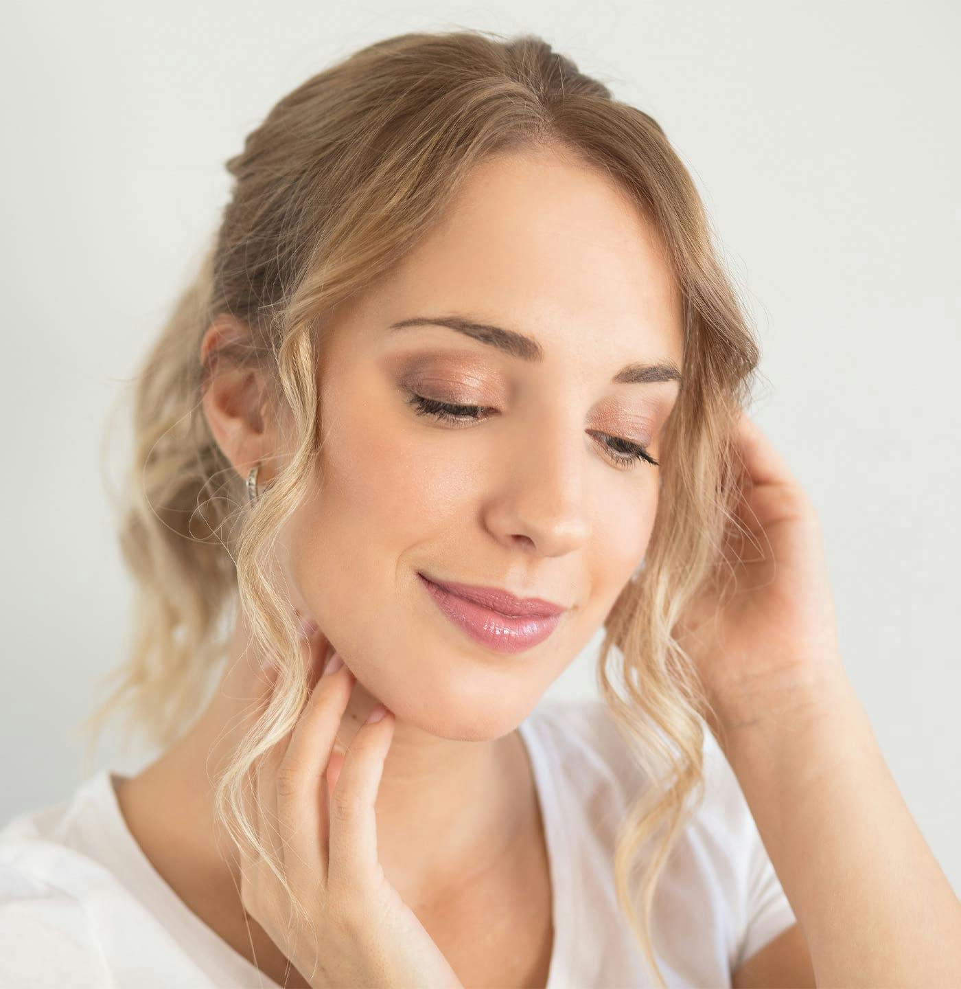 Woman smiling and looking down while touching neck and hair