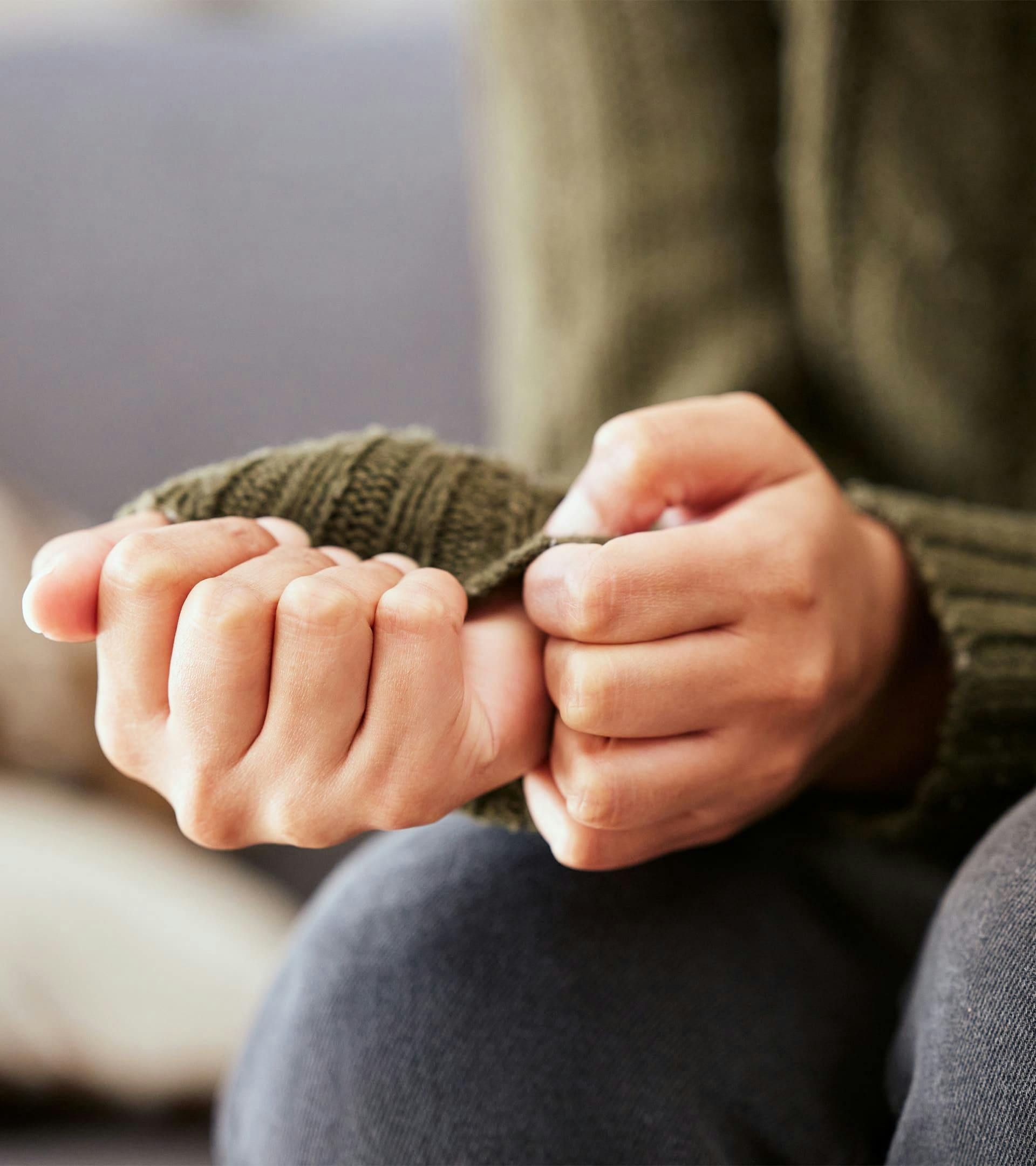 A person wearing a sweater with their hands together