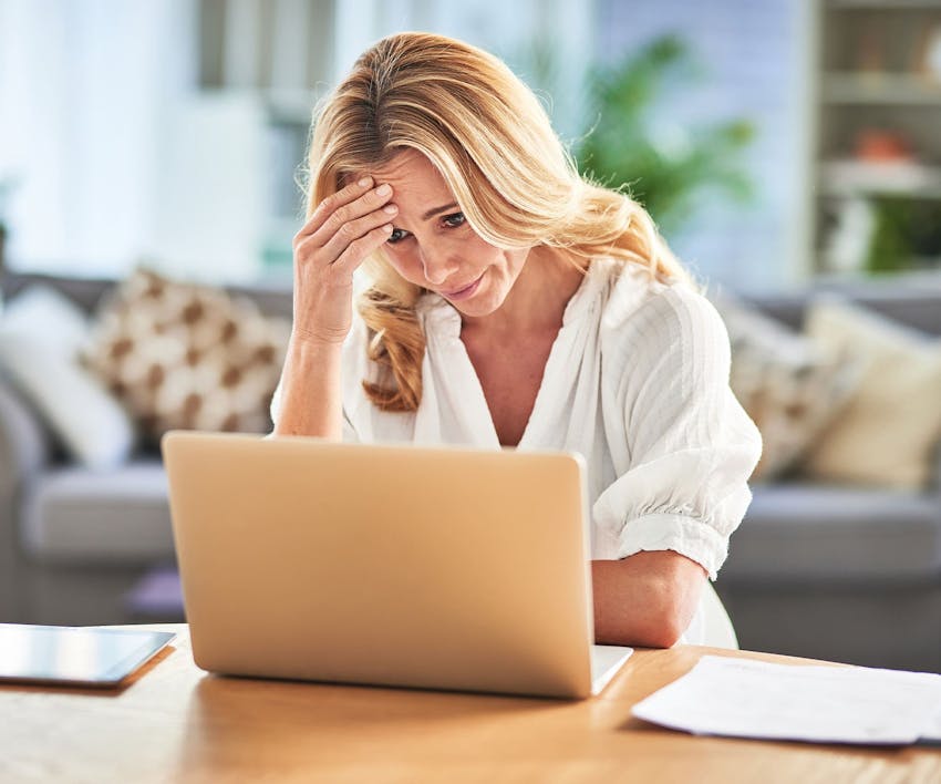 Woman looking at laptop rubbing forehead