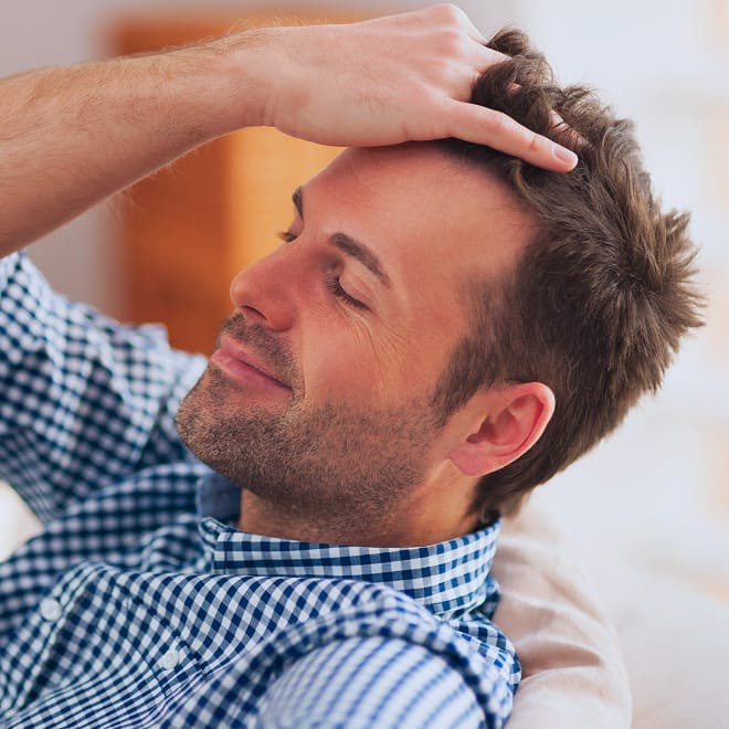 man brushing his hair back as he lies on the couch