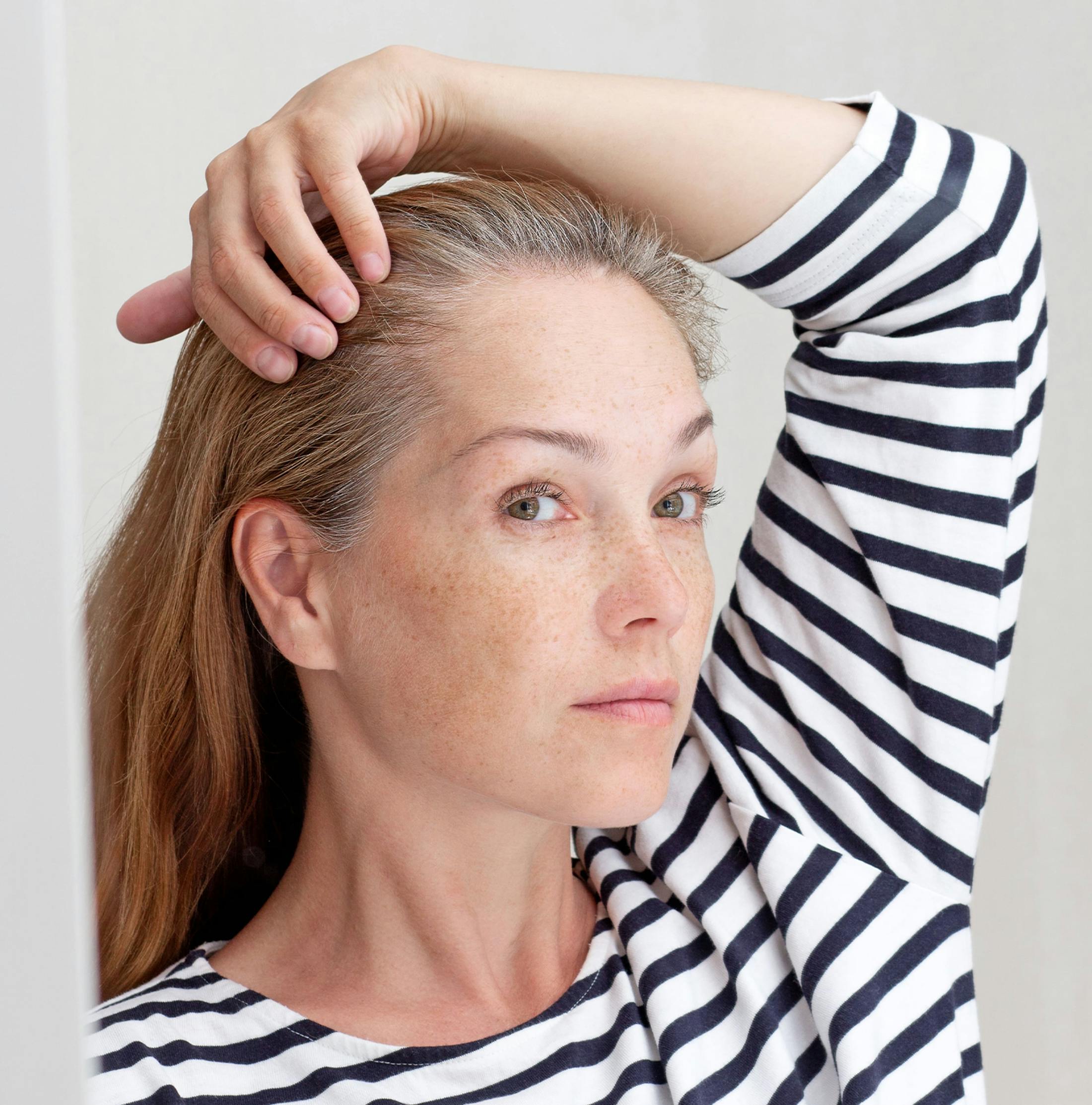 woman looking into mirror checking her hair line