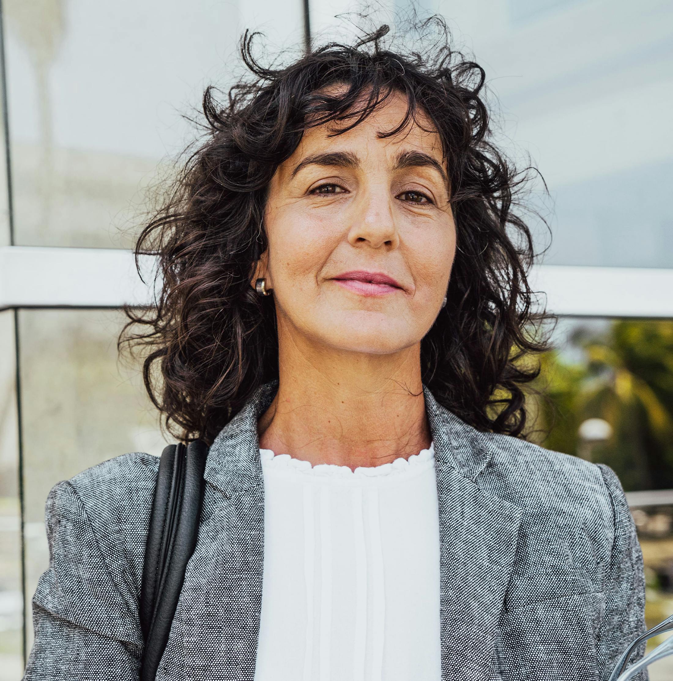 woman with very wavy hair outside building and smirking