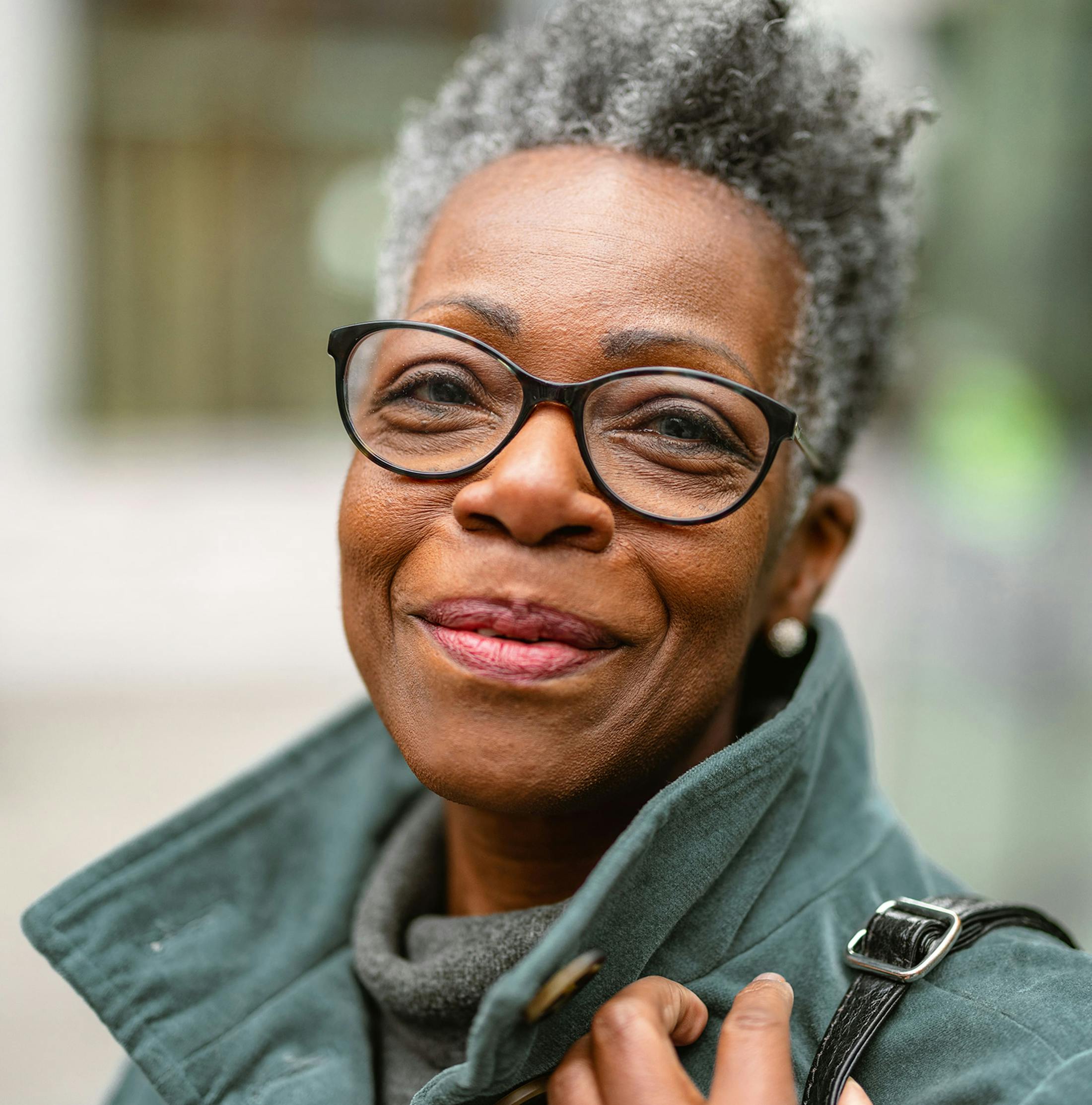 woman wearing glasses grinning with her hand hold her purse strap on her shoulder