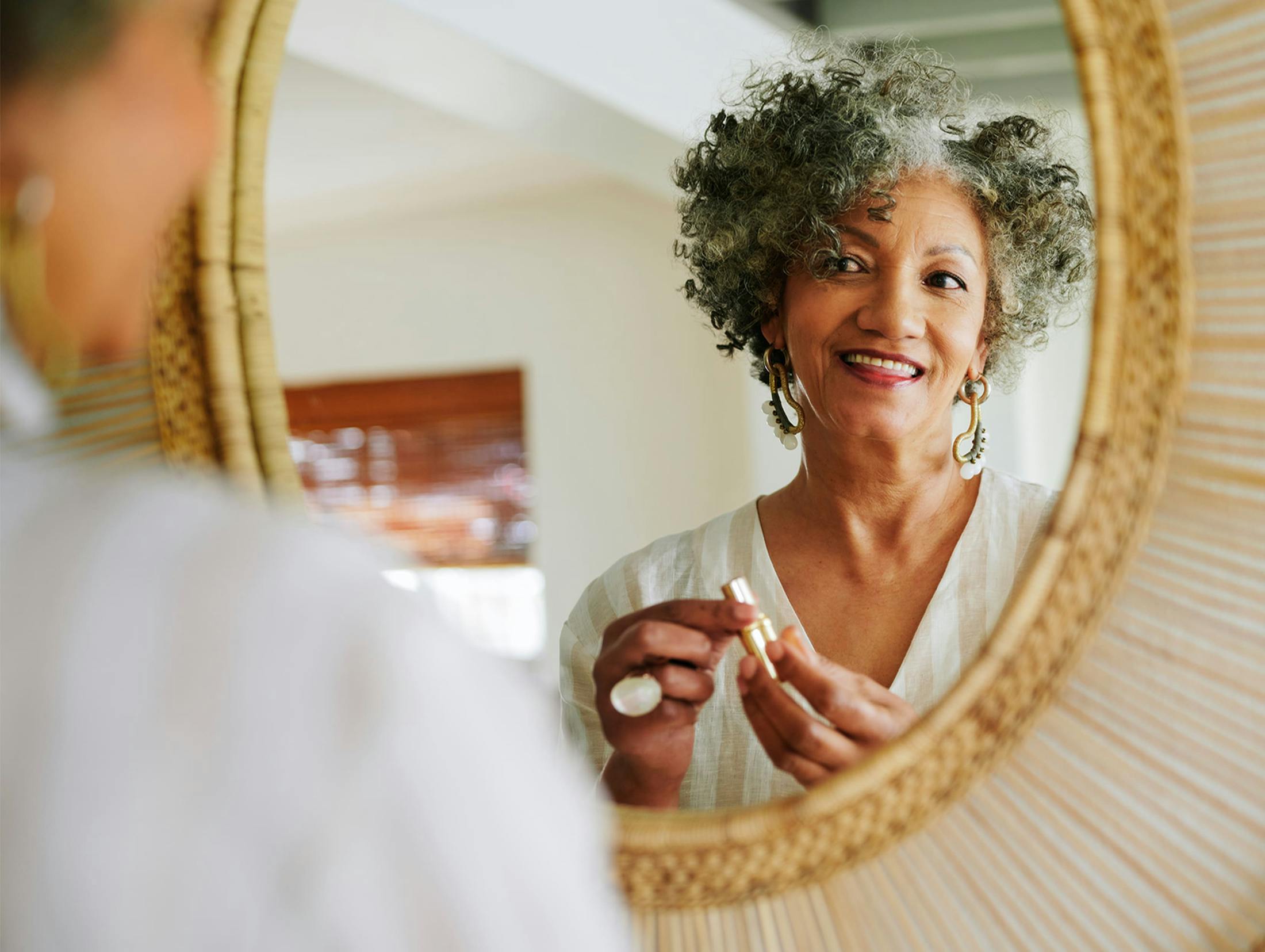 woman looking at herself in the mirror as she holds her lipstick