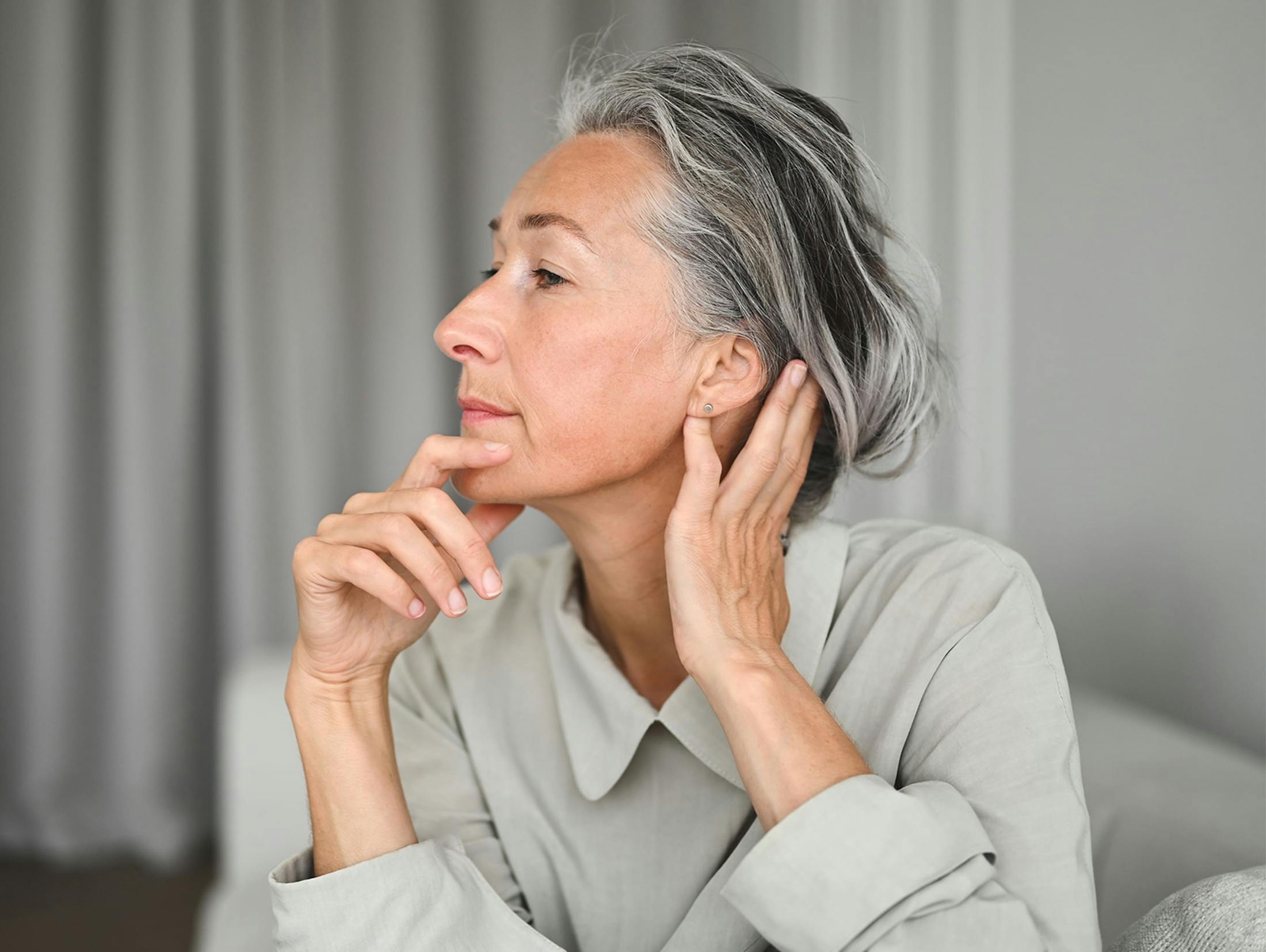 woman facing to the side with her hand behind her head and other touching her chin