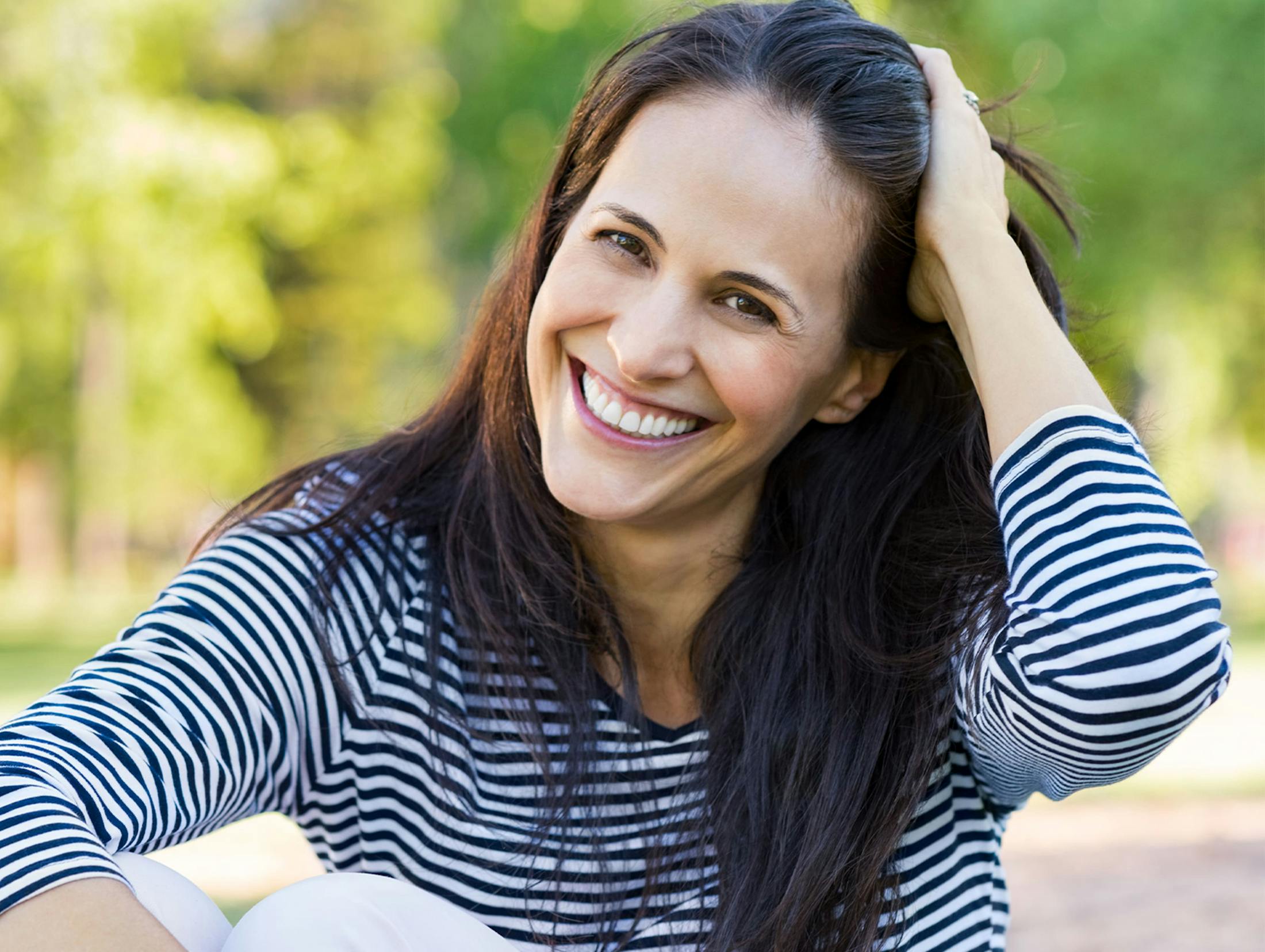 woman smiling and sitting outside and moving her hair back